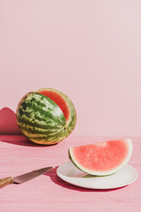 close up view of slice of watermelon on plate and knife on pink background