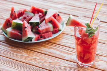 close up view of refreshing watermelon drink with mint in glass and pieces of fresh watermelon on wooden surface