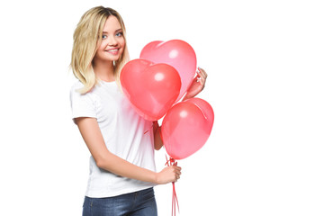 smiling attractive girl in white shirt holding bundle of heart shaped balloons isolated on white