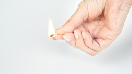 older womans hand holding a burning matchstick
