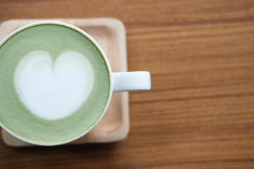 hot matcha green tea with heart latte art on wood table