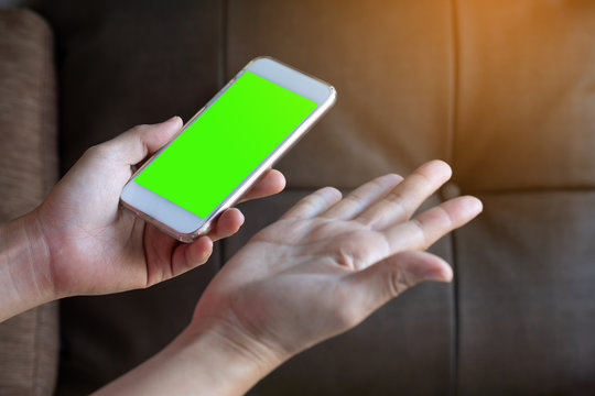 woman hand holding the smartphone with green screen on liveing room background.