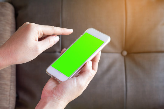 woman hand holding the smartphone with green screen on liveing room background.
