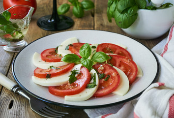 Italian salad with tomatoes, mozzarella and basil leaves on a grey plate
