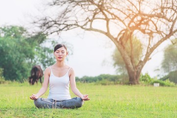 Young lady doing yoga exercise in green field outdoor area showing calm peaceful in meditation mind - people practise yoga for meditation and exercise concept