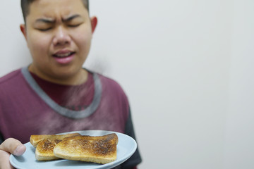 asian boy show over roasted burnt grilled bread dish with bad unhappy mood face - food breakfast disappoint concept