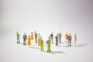 A big group of miniature business people stand on gray background.