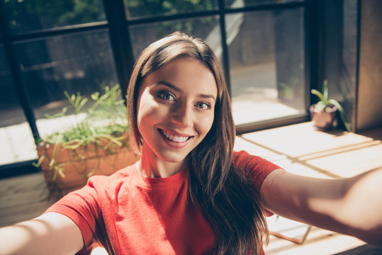 Kind and lovely young woman in a red T-shirt makes selfie from two hands to the front camera of her smartphone
