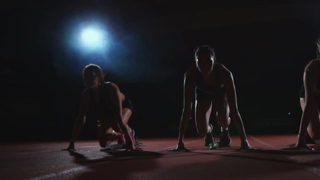 Three Girls In Black Clothes Are In The Starting Pads To Start The Race In The Competition In The Light Of The Lights And Run Towards The Finish