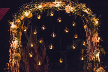 Night wedding ceremony, arch on party decorated with lights and candles in round glass spheres
