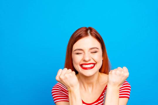 Portrait of nice vivid girlish red straight-haired happy smiling toothy young girl celebrating lottery victory winning, closed eyes, isolated over blue background