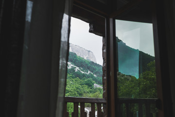 Mountain view through open window on balcony, rocks in cloudy and foggy weather