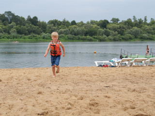Smiling boy in orange life vest running on the beach