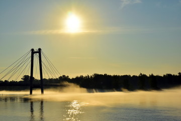 Fototapeta na wymiar Beautiful landscape. Fog over the river at sunrise. Silhouette of a cable-stayed bridge. Reflection of the sun in water. Krasnoyarsk. Siberia. Russia. Yenisei