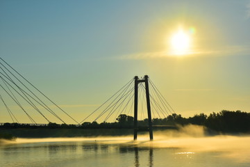 Beautiful landscape. Fog over the river at sunrise. Silhouette of a cable-stayed bridge. Reflection of the sun in water. Krasnoyarsk. Siberia. Russia. Yenisei