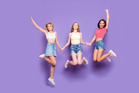 Portrait of foolish playful girls holding hands jumping in air enjoying vacation celebrating achievement isolated on vivid violet background