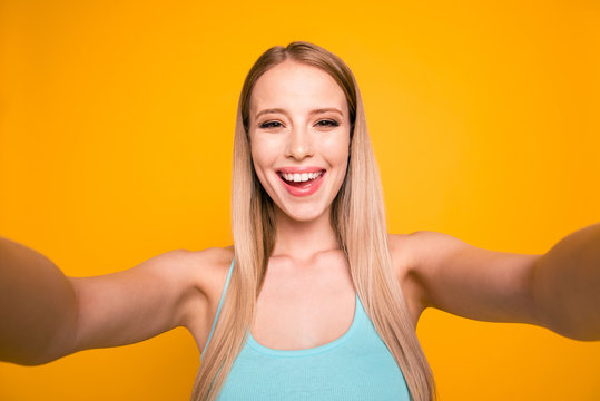 Self-portrait of cheerful cute straight-haired blonde caucasian girl, isolated over yellow background