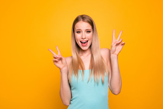 Portrait of young girl with blond hair and toothy beaming smile show v-sign isolated on bright yellow background