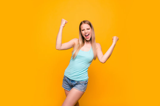 Yes, they did it! Happy blond girl raises her hands in fist isolated on vivid yellow background with copy space for text