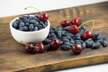 Fresh ripe honeysuckle berries and cherry in a ceramic bowl on a wooden board. Healthy breakfast. White bowl of honeysuckle.