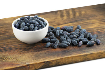 Fresh ripe honeysuckle berries in a ceramic bowl on a wooden board. Healthy breakfast. White bowl of honeysuckle.