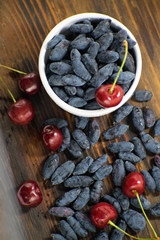 Fresh ripe honeysuckle berries and cherry in a ceramic bowl on a wooden board. Healthy breakfast. White bowl of honeysuckle.