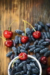 Fresh ripe honeysuckle berries and cherry in a ceramic bowl on a wooden board. Healthy breakfast....