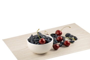 Fresh ripe honeysuckle berries and cherry in a ceramic bowl on a wooden board. Healthy breakfast. White bowl of honeysuckle.