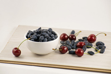 Fresh ripe honeysuckle berries and cherry in a ceramic bowl on a wooden board. Healthy breakfast. White bowl of honeysuckle.