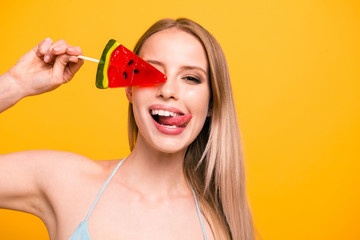 Close up portrait of girl with long blond hair covers her eyes with caramel candy on a stick...