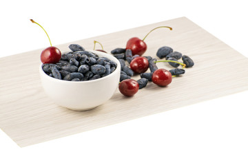 Fresh ripe honeysuckle berries and cherry in a ceramic bowl on a wooden board. Healthy breakfast....