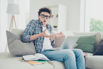 Handsome curly-haired confused young guy student nerd, wearing casual, sitting of sofa at home,...