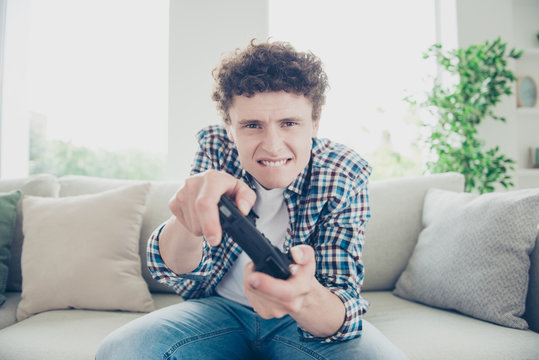 Attractive curly-haired tense nervous young guy student wearing casual, sitting of sofa at home, playing video game