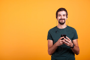 Happy smiling man with headphones on listening music on his smartphone isolated on yellow background. Mobile entertainment lifestyle