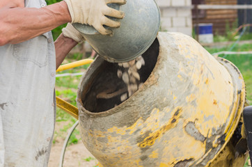 construction worker makes concrete in rotating concrete mixer. process of creating cement on the...