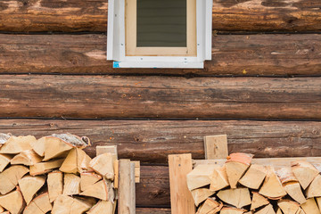 two stacks of firewoods near log wall under the window. outdoor storage of woodpile