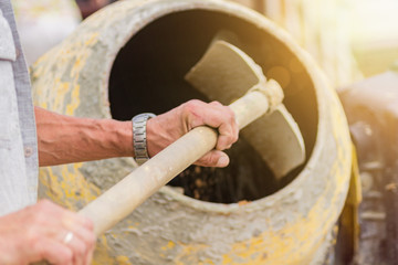 construction worker shovels the sand into the concrete mixer. process of creating cement on the...