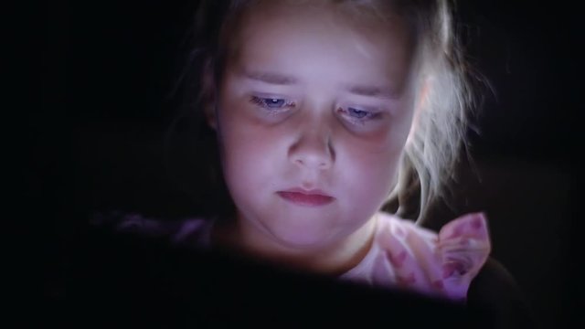 Portrait of little child girl using tablet technology in bed by night at home, close-up