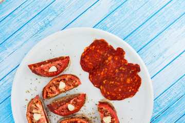 Freshly Cooked Little Sandwiches With Brown Bread Smoked Salami Fresh Bio Organic Tomatoes And Garlic On White Big Dish On Wooden Blue Surface