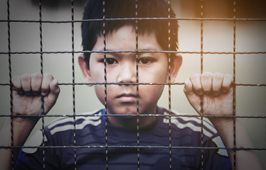 Dark portrait of a boy stand behind and holding steel screen or chain link fence - stressed sad...