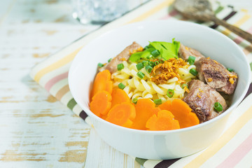 Macaroni soup with pork and carrot on white wooden table - delicious and healthy food concept