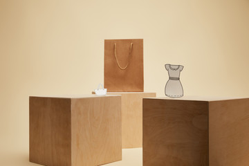 shopping bag, paper bag and paper dress on wooden cubes isolated on beige