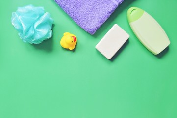 Baby bath products/ Flat lay photo blue sponge, yellow rubber duck, soap bar and shampoo on a green background