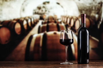 a glass and a bottle of wine on the background of barrels