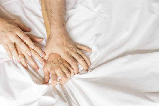 Couple having sex. Hand clutches grasps a white crumpled bed sheet in a hotel room, a sign of ecstasy, feeling of pleasure or orgasm