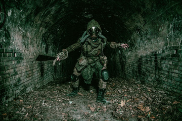 Post apocalyptic mutant creature or survivor in tatters and gas mask jumps out of darkness and...