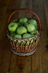 Wicker basket with morning harvest of green apples, on a wooden table. Healthy food, agriculture, summer garden.