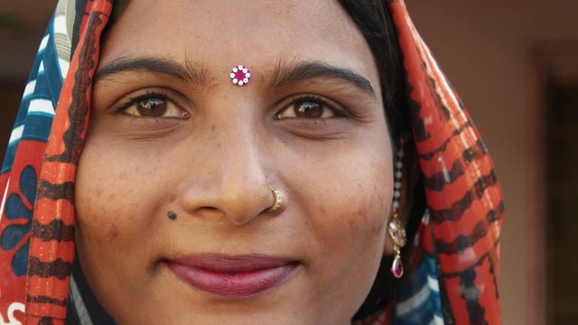 Extreme close up of a gorgeous Indian woman's face smiling laughing happy joy jovial looking at camera in traditional dress head covered bindi pretty jewelry at home freedom love static shot lock down