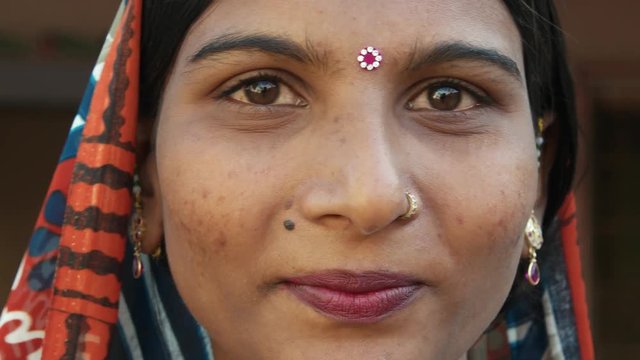 Extreme close up of a gorgeous Indian woman's face smiling laughing happy joy jovial looking at camera in traditional dress head covered bindi pretty jewelry at home freedom love static shot lock down
