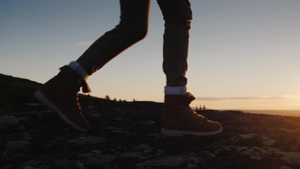 Legs in trekking boots go along the mountain ridge against the backdrop of the rising sun. Travel and adventure concept